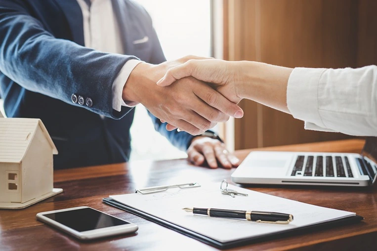 A person shaking hands with their attorney after negotiating a cash settlement with the insurance company over a desk that has a laptop and clipboard on it.